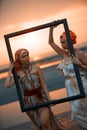 Girls traveler with wooden picture frame at colorful sea sunset