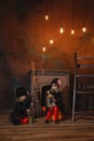 Girls in witch costumes are sitting near the fireplace on pumpkins, one is holding a lantern, the other is making a potion Royalty Free Stock Photo