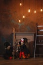 Girls in witch costumes are sitting near the fireplace on pumpkins, one is holding a lantern, the other is making a potion Royalty Free Stock Photo