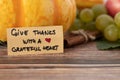 Give thanks with a grateful heart, a handwritten text on a vintage card with various autumn fruit in the background