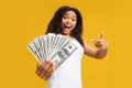 Giveaway concept. Excited young black woman holding a lot of dollar cash, showing big win over yellow studio background