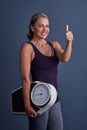 Giving exercise a big thumbs up. Studio portrait of an attractive mature woman holding a weightscale and giving thumbs Royalty Free Stock Photo