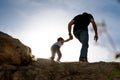 Young father giving helping hand to his son walking over mountain top as a metaphor of fatherhood