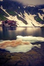 A glacial lake with some ice cap on it set high above in the mountains with a house on the shore in Romania