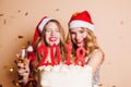 Glad blonde girl in santa claus costume holding new year cake on light background. Indoor photo of happy friends