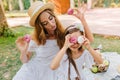 Glad blonde woman with light makeup looking with love at daughter playing with cookies. Outdoor portrait of little girl