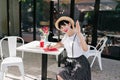 Glad brunette girl writes in notebook and waving hand with smile, resting in cafe. Outdoor portrait of laughing female Royalty Free Stock Photo