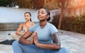 Glad calm young middle eastern and african american women athletes in sportswear with closed eyes practice yoga