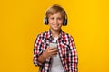 Glad caucasian adolescent boy in headphones holding smartphone, chatting