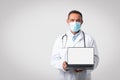 Glad caucasian mature doctor in white coat, protective mask show laptop with empty screen