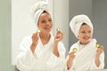 Glad caucasian small girl and young lady in bathrobe and towel, have fun with pieces of cucumber enjoy beauty care Royalty Free Stock Photo