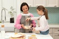 Glad caucasian young mother and little daughter make cookie dough, enjoy prepare eat at spare time