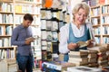 Glad elderly woman reading book in book shop