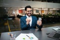 Glad emotional young middle eastern businessman with beard in glasses and suit looks at smartphone