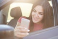 Glad European female with long dark hair, happy to recieve message on smart phone, poses in car, stops on road, connected to wirel Royalty Free Stock Photo