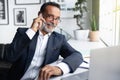 Glad european senior businessman in suit, glasses with laptop calls by smartphone at table in office