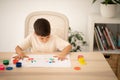 Glad european small kid draws picture with hands and paints at table in kindergarten, school or living room