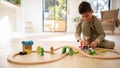 Glad european small kid in pajamas plays with toys, train, cars and wooden road, enjoy spare time