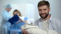 Glad father holding newborn, obstetrician explaining mother how to breast-feed