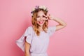 Glad girl in cute wreath posing on bright background with peace sign. Indoor portrait of pleased curly woman with flower