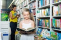 Glad girl in school age looking in open chosen book