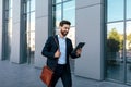 Glad handsome confident young caucasian guy with beard in suit chatting on tablet, goes to work