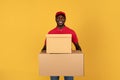 Glad handsome millennial black guy courier in red uniform hold many big boxes for delivery
