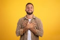 Glad handsome young european man presses hands to chest, isolated on yellow studio background