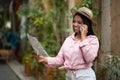 Glad happy young black lady in casual sunglasses looks at map calls on phone enjoys trip in new city, outside