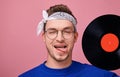 Glad hippie guy with protruding tongue and covered right eye in eyeglasses and black vinyl record Royalty Free Stock Photo