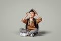 Glad little european boy with backpack puts book on head, sits on floor, enjoy learning Royalty Free Stock Photo