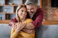 Glad middle aged european male hugs woman, enjoy comfort and romance on sofa in cozy living room