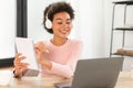 Glad millennial african american woman in wireless headphones shows notebook to webcam laptop