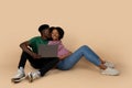 Glad millennial black husband kissing wife on cheek, enjoy pregnancy, use laptop, sit on floor