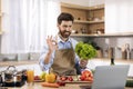 Glad millennial caucasian male cooking eat show salad and ok hand sign at table with vegetables and computer Royalty Free Stock Photo