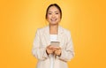 Glad millennial chinese businesswoman in suit, typing on smartphone for business