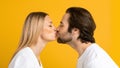 Glad millennial european guy and woman in white t-shirts kiss and enjoy tender moment together