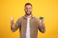 Glad millennial european man with beard show credit card, use phone, celebrate success victory