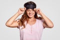 Glad optimistic Caucasian woman wears eye mask, has broad smile, dressed in pyjamas, has happy expression, sees pleasant dreams, Royalty Free Stock Photo