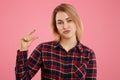 Glad positive female with appealing look shows something tiny with fingers, dressed in checkered shirt, isolated over pink backgro