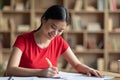 Glad pretty busy smart japanese female make notes at table, prepare for exam test in living room interior Royalty Free Stock Photo