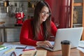 Glad professional brunette female accountant makes distant work, keyboards on laptop computer, sits at kitchen table Royalty Free Stock Photo