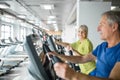 Glad senior lady training on stair stepper at gym with friend