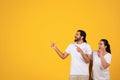 Glad shocked millennial arab couple pointing fingers at empty space, for text or ad