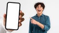 Glad shocked surprised millennial european man pointing finger at hand with smartphone with empty screen