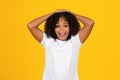 Glad shocked teenage black schoolgirl in white t-shirt with open mouth, isolated on yellow background