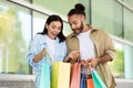 Glad shocked young european woman and man looking at bags, enjoy shopping, purchases in mall