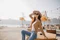 Glad slim girl in jeans sitting on wooden table in street restaurant. Outdoor photo of brunette woman in sunglasses Royalty Free Stock Photo