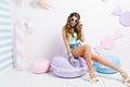 Glad slim girl with long legs sitting on big purple macaroon and laughing. Indoor portrait of pretty young woman in Royalty Free Stock Photo