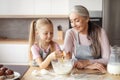 Glad Smiling Little Girl And Senior Woman In Aprons Make Dough, Break Egg In Minimalist Kitchen Interior